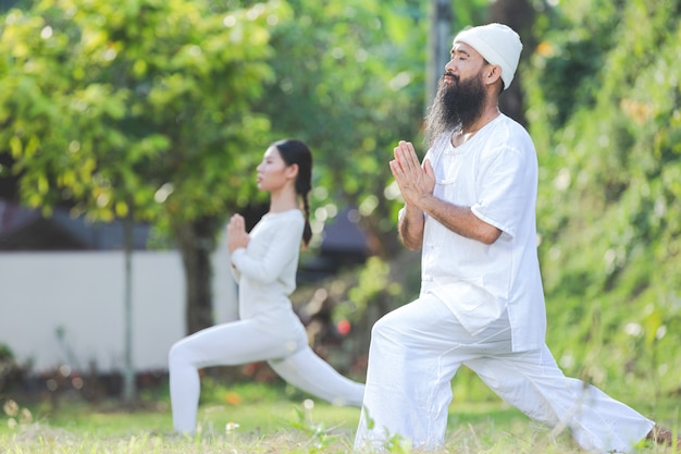 Duas pessoas vestidas de branco fazendo ioga na natureza