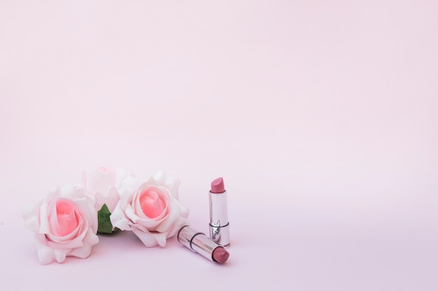 Foto grátis duas rosas e batons no pano de fundo rosa
