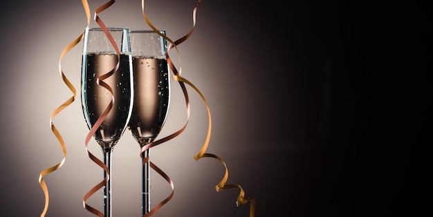 Duas taças cheias de champanhe prontas para a festa. imagem em um fundo escuro com luz de fundo e espaço de cópia