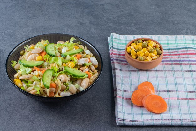 Duas tigelas de salada de legumes e cenoura fatiada em um pano de prato, na superfície de mármore