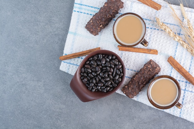 Duas xícaras de café com folha de papel e chocolates na toalha de mesa.