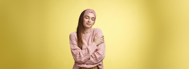 Foto grátis dulce e glamourosa jovem vestindo uma camisola quente e confortável abraçando-se cruzando os braços sobre o corpo em abraço