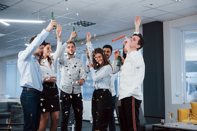 Foto grátis É assim que o sucesso se parece. foto da equipe jovem em roupas clássicas, comemorando o sucesso enquanto segura bebidas no moderno escritório iluminado bom