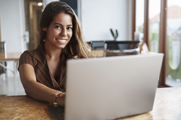 e uma mulher hispânica de sucesso sorrindo usando laptop no café