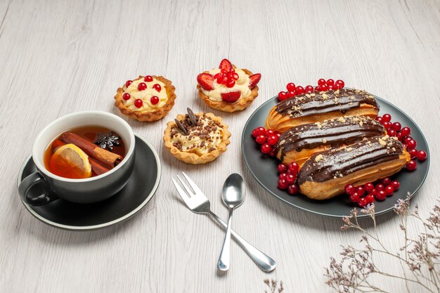 Éclairs de chocolate e groselha na placa cinza cookies limão canela colher de chá e garfo em vetor diagonal na mesa de madeira