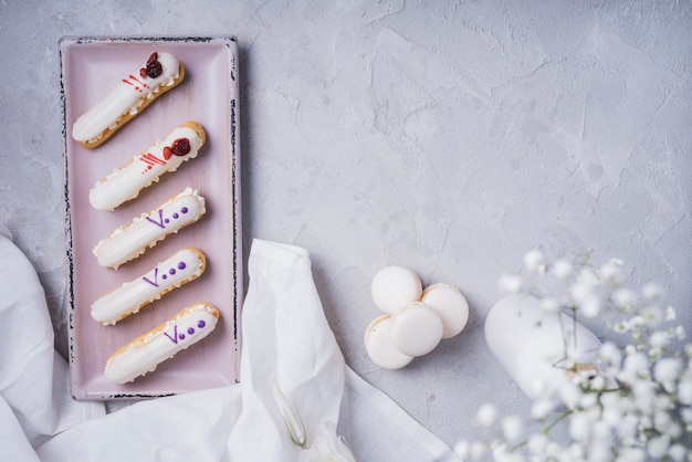 Foto grátis eclairs de creme com macaroons e vaso de flores de respiração do bebê