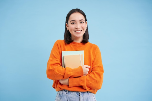 Foto grátis educação e estudantes feliz mulher asiática segurando cadernos e rindo sorrindo para a câmera gosta de goi