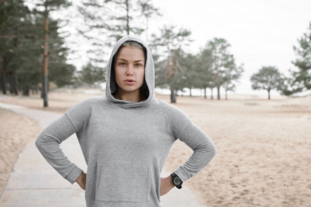 Elegante corredor feminino europeu se preparando para a maratona, fazendo a rotina de atividade cardiovascular matinal na floresta. Jovem desportiva autodeterminada confiante a treinar ao ar livre, de mãos dadas na cintura