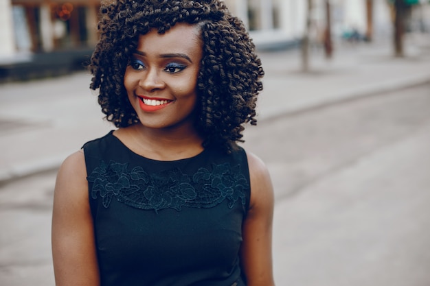 Foto grátis elegante e elegante garota de pele escura com cabelo encaracolado andando pela cidade de verão