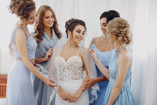 Elegante e elegante noiva junto com seus quatro amigos em vestidos azuis em pé em um quarto