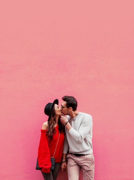 Elegante elegante casal apaixonado, de mãos dadas e olhando um ao outro com prazer. mulher de cabelos longos na camisola de malha vermelha com o namorado dela posando.