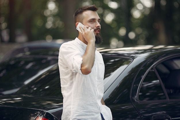 Elegante empresário em pé perto do carro e usar telefone celular