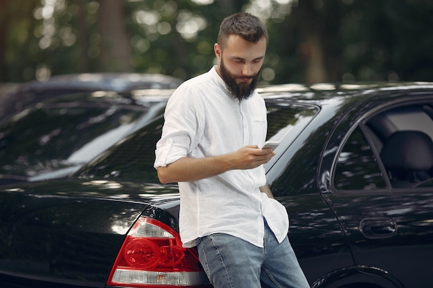 Elegante empresário em pé perto do carro e usar telefone celular