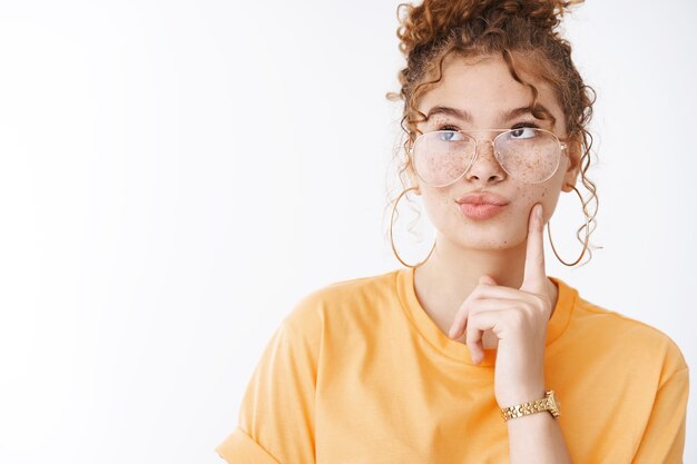 Elegante glamour atrevido jovem ruiva feminina usando óculos camiseta laranja dobrando lábios fazendo beicinho olhar pensativo canto superior esquerdo pensando lembrar número entrega serviço fazer escolha mente