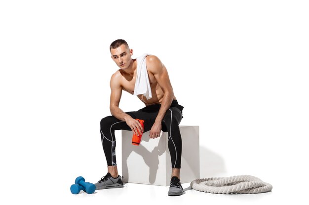 Elegante jovem atleta do sexo masculino praticando no fundo branco do estúdio, retrato com sombras. Modelo de ajuste esportivo para exercícios em movimento e ação.