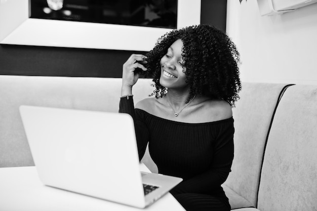 Elegante jovem e bela empresária afro-americana com penteado afro vestindo elegante preto sentado e trabalhando no laptop