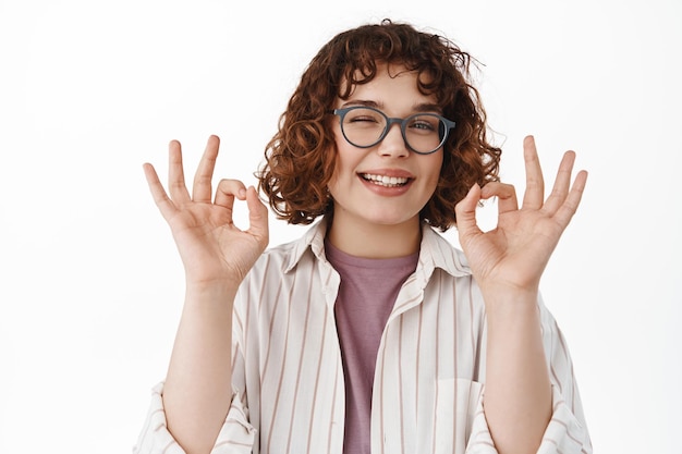 Elegante jovem elogiar algo de bom, mostrando sinais de ok e piscando, acenar em aprovação, satisfeito com a grande qualidade, fazer elogios, de pé sobre fundo branco.