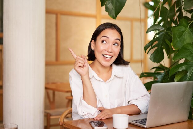 Elegante jovem empreendedora com laptop sentado no café, apontando o dedo para o banner de propaganda