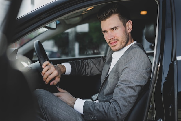 Elegante jovem empresário sentado no carro com uma porta aberta