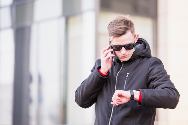 Elegante jovem falando no celular, olhando a hora em seu relógio de pulso