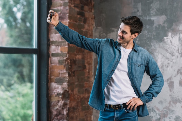 Elegante jovem posando em frente a janela tomando selfie do celular