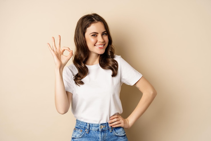 Foto grátis elegante jovem sorrindo satisfeita, mostrando ok, ok sinal de aprovação, recomendando, de pé sobre fundo bege