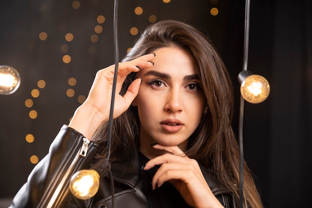 Elegante menina bonita com roupas de couro preto sobre um fundo de lâmpadas no estúdio.