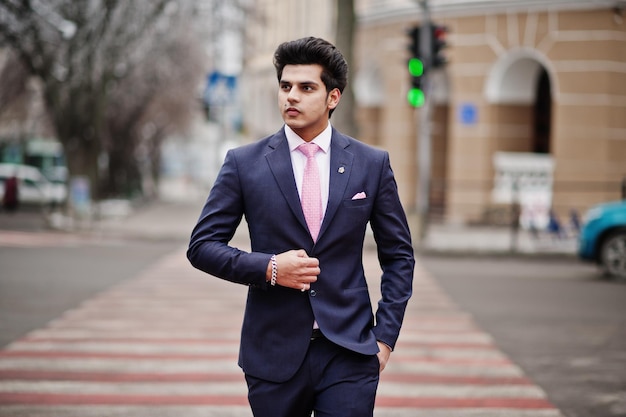 Elegante modelo de homem macho indiano de terno e gravata rosa andando na travessia de pedestres