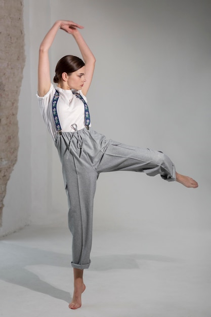Elegante modelo feminino dançando no estúdio em elegante camisa branca e suspensórios. novo conceito de feminilidade