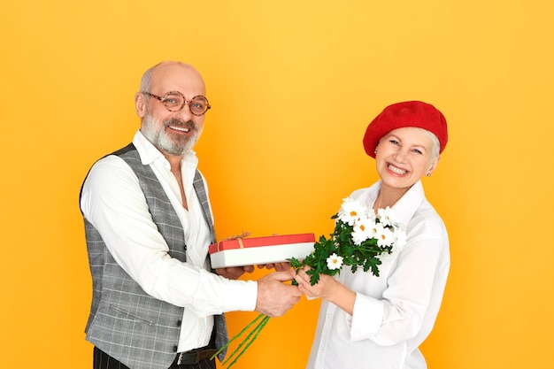 Elegante reformado careca com a barba por fazer e óculos dando um presente de aniversário para sua adorável esposa de meia-idade