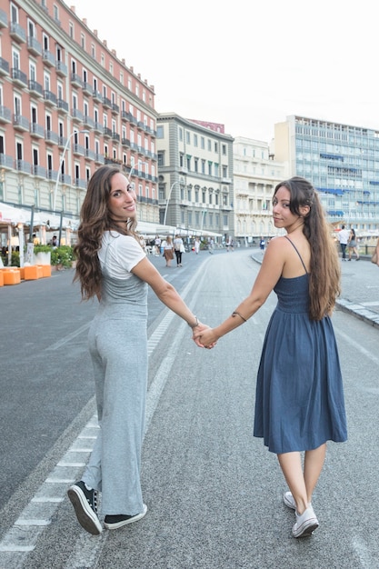 Elegantes mulheres jovens andando na rua, segurando a mão do outro