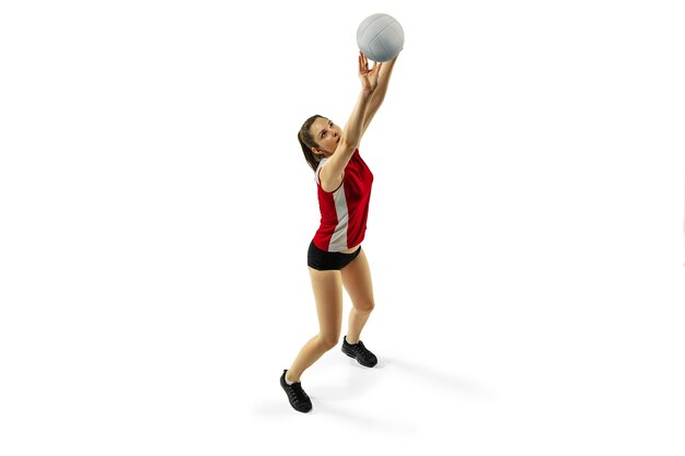 Em salto e vôo. Jovem jogadora de voleibol isolada no fundo branco do estúdio. Mulher em roupas esportivas e tênis, treinando, jogando. Conceito de esporte, estilo de vida saudável, movimento e movimento.