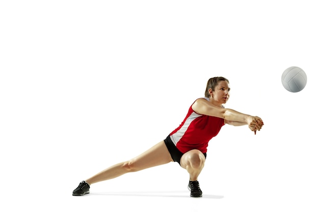 Em salto e vôo. jovem jogadora de voleibol isolada no fundo branco do estúdio. mulher em roupas esportivas e tênis, treinando, jogando. conceito de esporte, estilo de vida saudável, movimento e movimento.