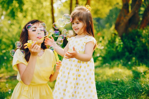 em um parque de verão perto de árvores verdes, a mãe anda em um vestido amarelo e sua menina bonita