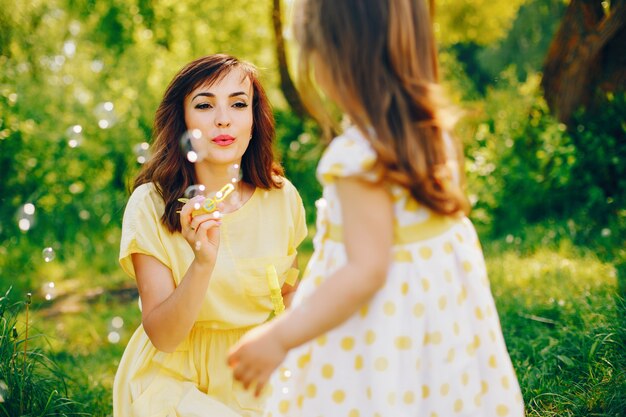 em um parque de verão perto de árvores verdes, a mãe anda em um vestido amarelo e sua menina bonita