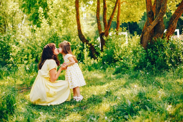 em um parque de verão perto de árvores verdes, a mãe anda em um vestido amarelo e sua menina bonita