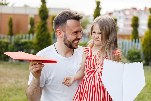 Emocional sorridente pai e filha com aviões de papel ao ar livre