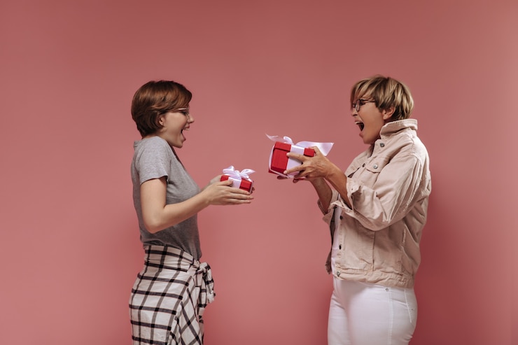 Foto grátis emocionantes mulheres com cabelo curto e óculos em roupas modernas, segurando caixas de presente vermelhas e regozijando-se no fundo rosa isolado.