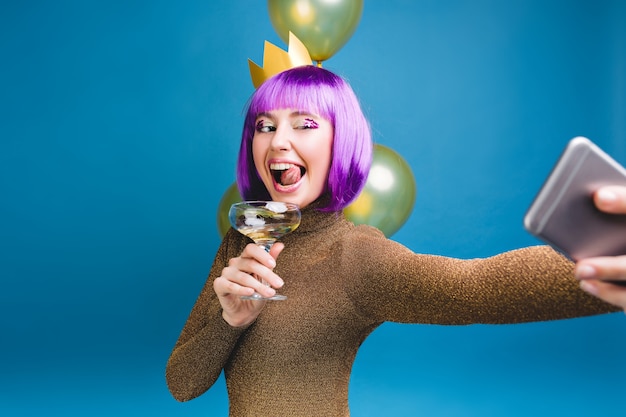 Foto grátis emoções brilhantes de celebração de jovem com corte de cabelo roxo, fazendo retrato de selfie. balões dourados, se divertindo, mostrando a língua, champanhe, festa de ano novo, aniversário.