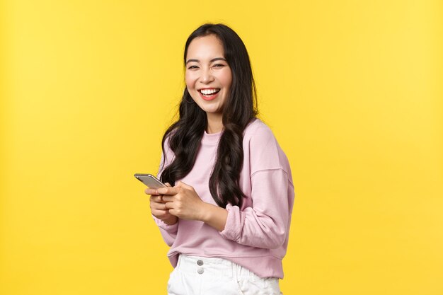 Emoções de pessoas, lazer do estilo de vida e conceito de beleza. Mulher asiática feliz sorridente alegre, vire para a câmera e rindo depois de ler uma postagem engraçada no aplicativo de mídia social, segurando o smartphone.