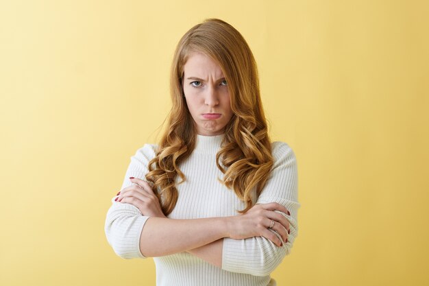 Emoções humanas negativas e expressões faciais. Jovem caucasiana caprichosa e irritada com uma elegante gola olímpica, franzindo a testa e cruzando os braços, irritada porque o marido não lhe dá graça