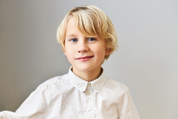 Emoções, reações e sentimentos humanos. Retrato de um estudante bonito bonito com cabelo loiro e olhos azuis posando isolado na camisa branca.