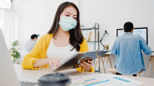 Empreendedor de empresária da ásia usando máscara médica para distanciamento social na nova situação normal para prevenção de vírus enquanto usa o laptop no trabalho no escritório. estilo de vida após o vírus corona.