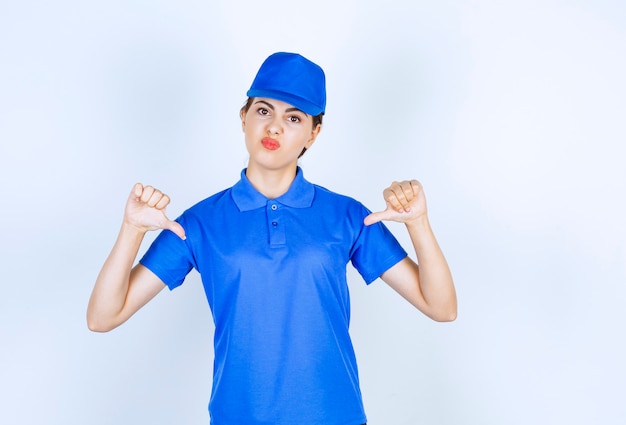 Empregada de entrega de mulher com uniforme azul em pé e apontando para si mesma.