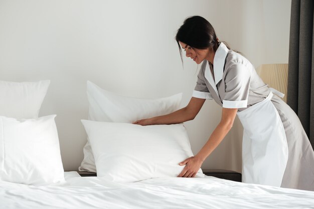 Empregada de hotel jovem configurar travesseiro na cama