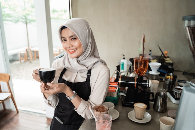 Empregada de mesa velada asiática sorrindo espera uma xícara de café
