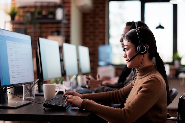 Empregado asiático paralisado trabalhando na recepção do call center em escritório amigável para deficientes. Operadora de cadeira de rodas com deficiência dando assistência na linha de atendimento ao cliente.