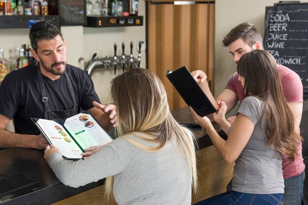 Empregado de bar ajudando o cliente do sexo feminino a olhar para o menu no balcão de bar