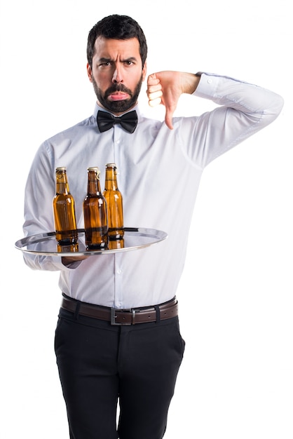 Empregado de mesa com garrafas de cerveja na bandeja fazendo sinal ruim