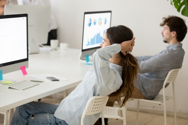 Empregado do sexo feminino relaxante do trabalho de computador, segurando as mãos atrás da cabeça